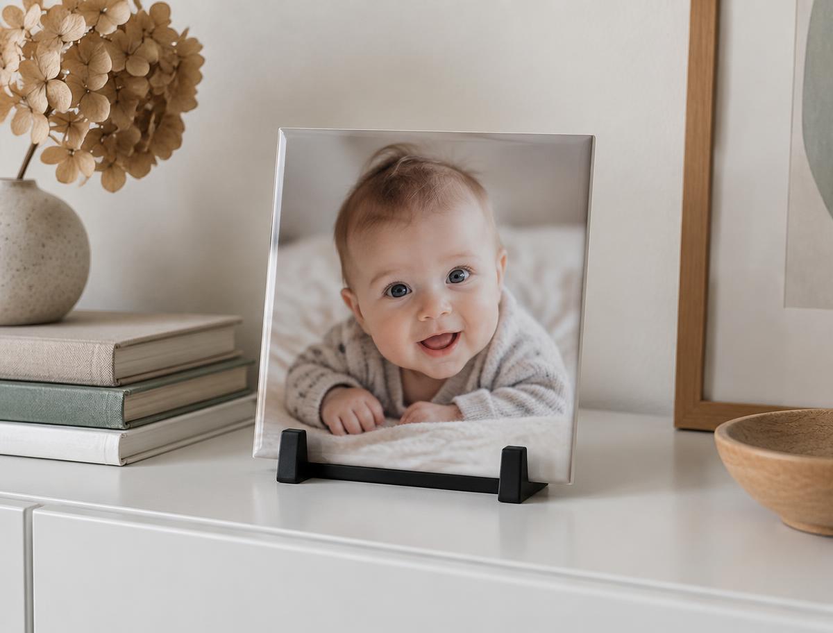Tegeltje met babyfoto in een zwarte standaard op een witte kast met boeken en droogbloemen